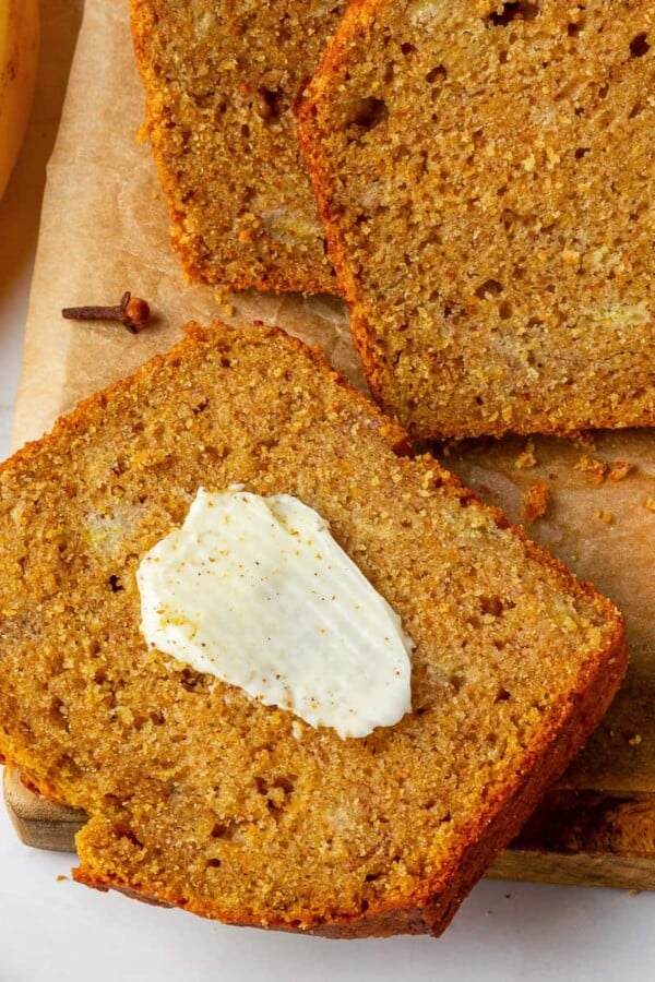 Slice of pumpkin banana bread spread with melting butter on warm crumb.