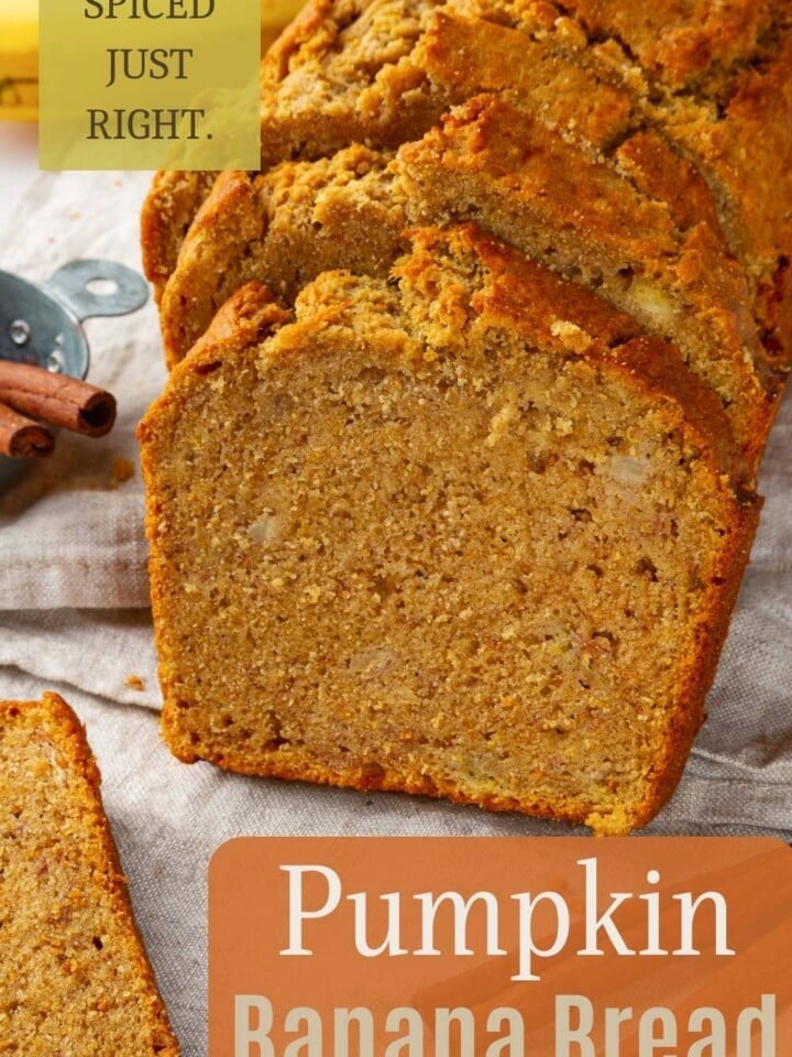 Pumpkin banana bread loaf on parchment paper, with cinnamon sticks beside thick, tender slices.