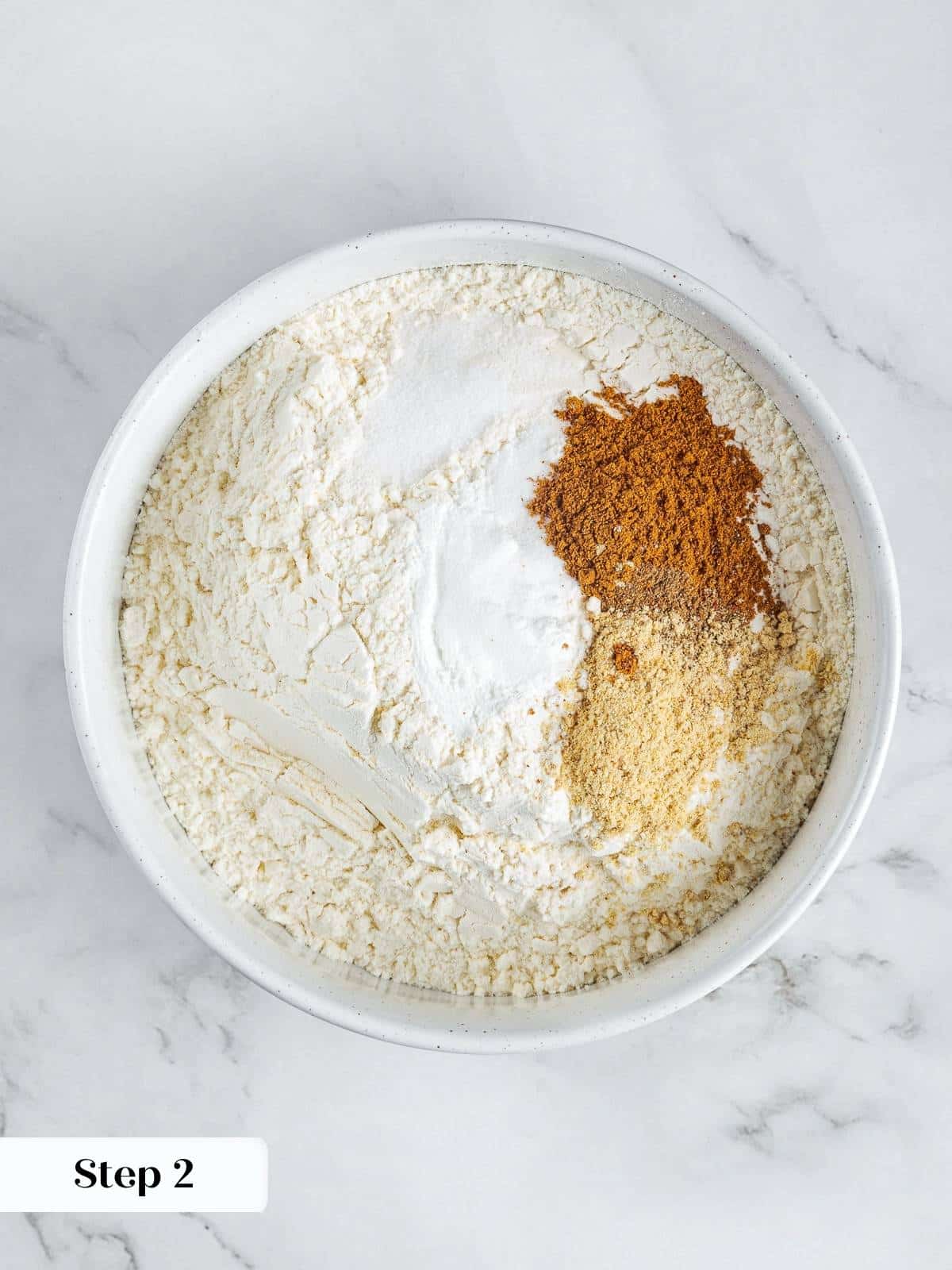 Mixing bowl filled with flour, cinnamon, nutmeg, and ginger for pumpkin banana bread.