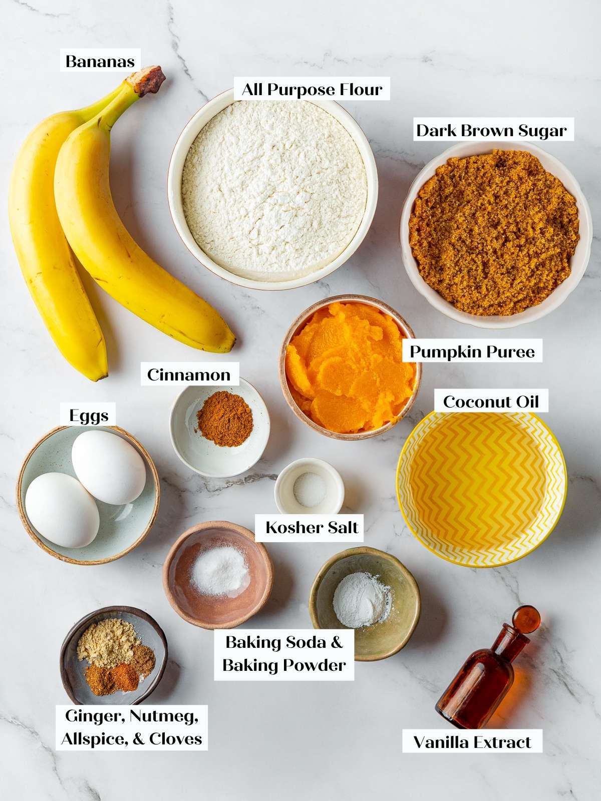 Countertop with flour, pumpkin puree, bananas, and spices arranged for making pumpkin banana bread.