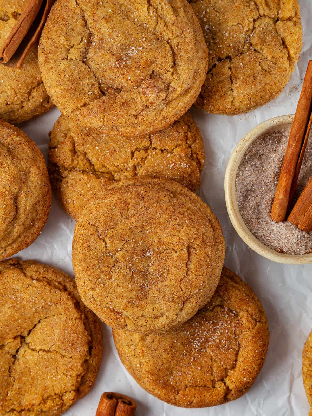 Several pumpkin snickerdoodles displayed on parchment, highlighting cinnamon sugar coating and chewy inside texture.