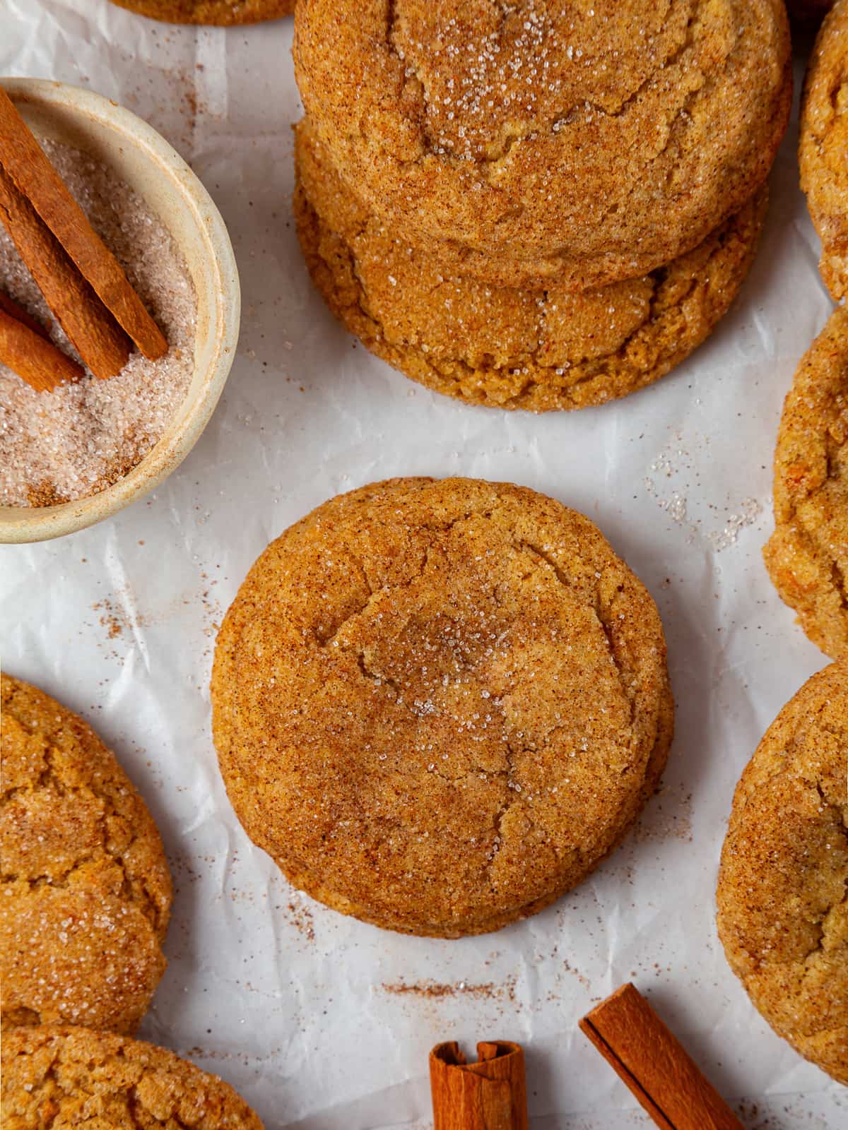 Freshly baked pumpkin snickerdoodles resting on parchment paper, showing chewy centers and crackled sugar crust.