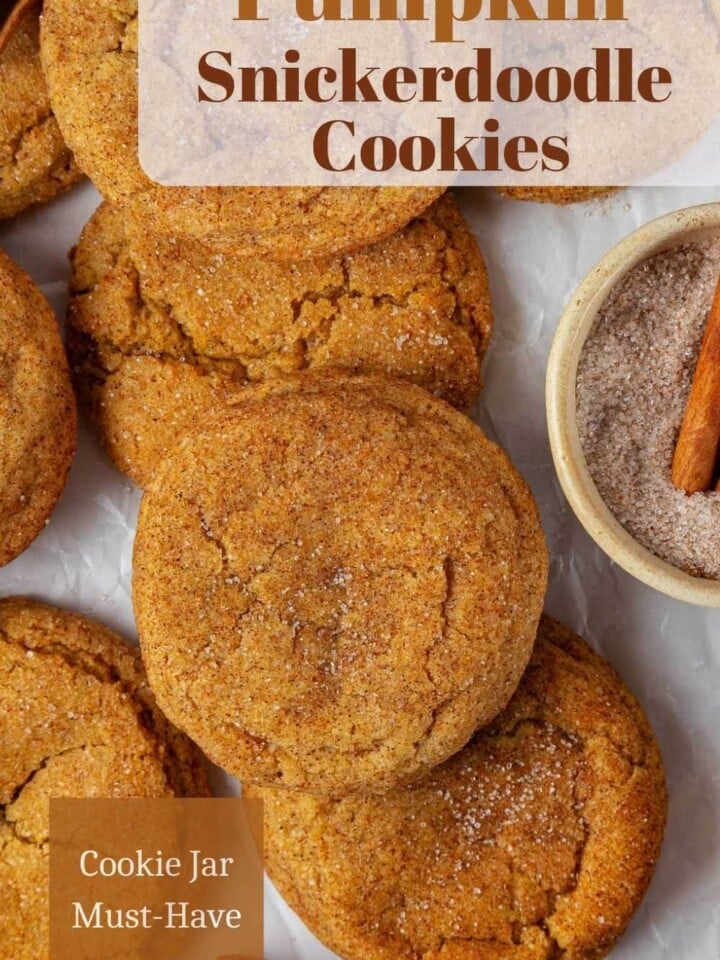 Golden pumpkin snickerdoodles covered in cinnamon sugar, resting on parchment, chewy inside with crisp edges.