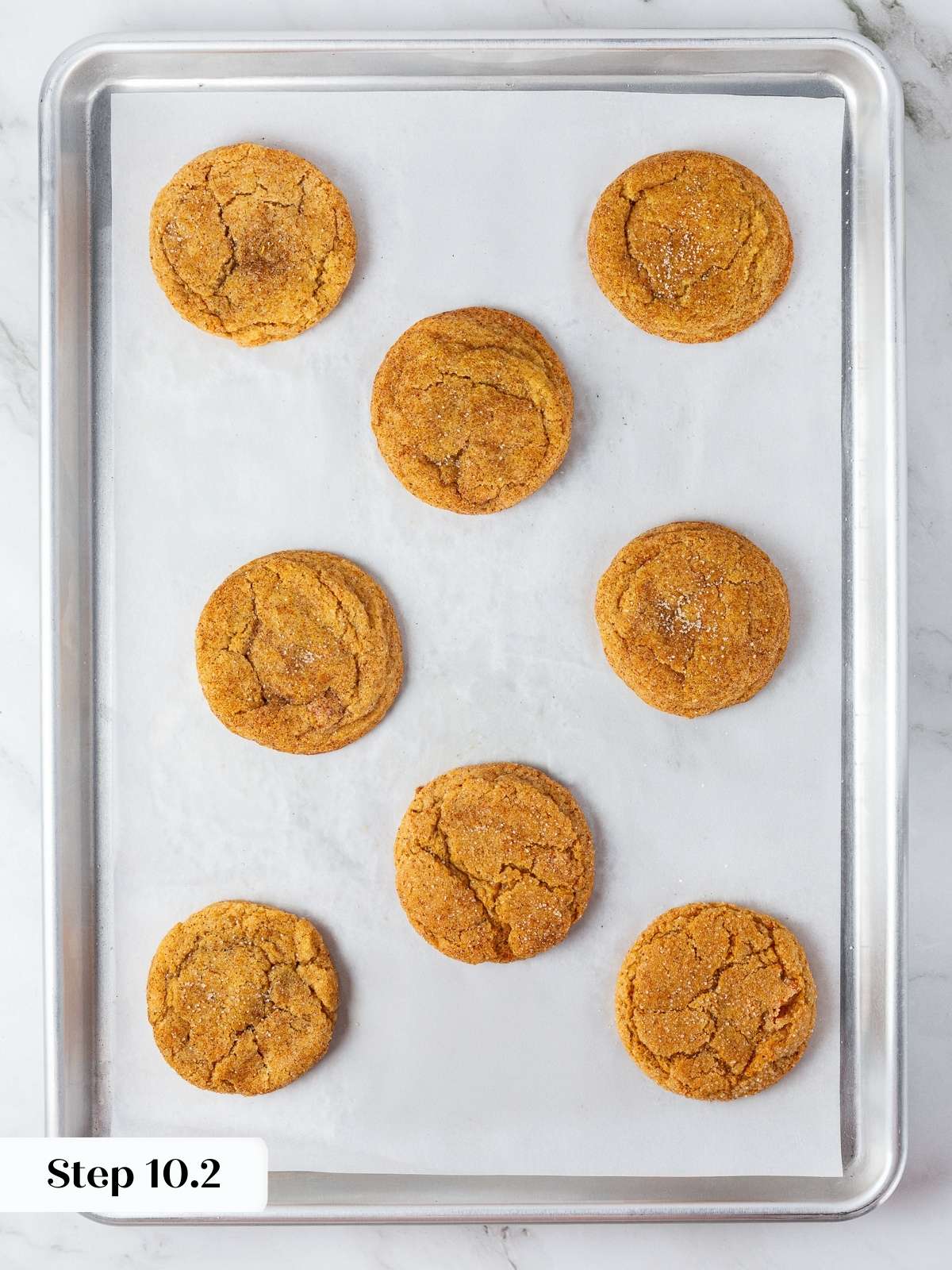 Pumpkin snickerdoodles finished baking, resting on parchment-lined sheet, featuring chewy centers and crisp edges.