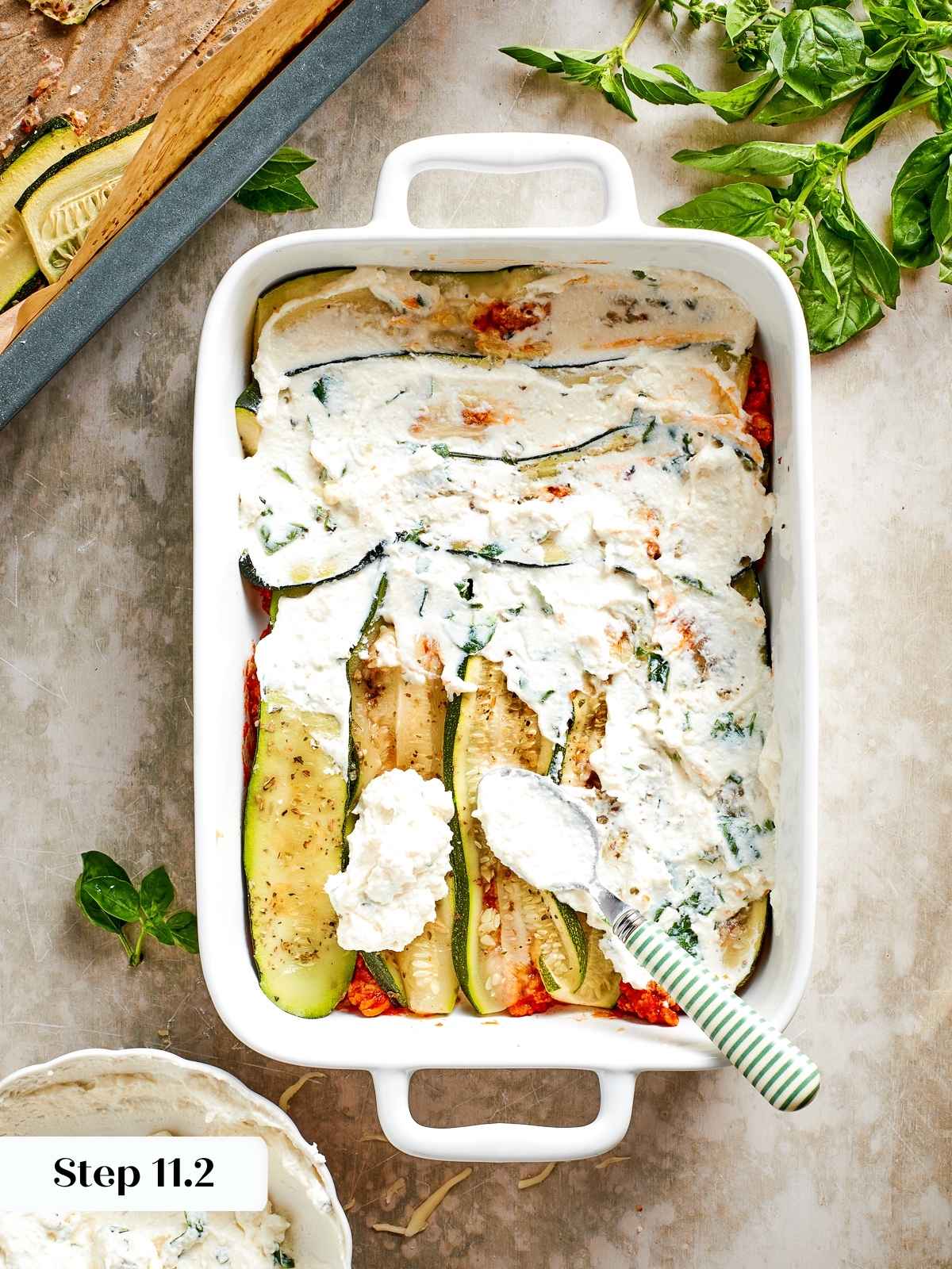 Herbed ricotta being spread onto roasted zucchini slices during the lasagna assembly process.