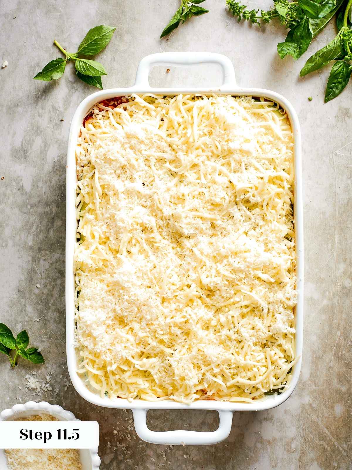 Final layer of shredded mozzarella being sprinkled generously over the top of assembled zucchini lasagna.
