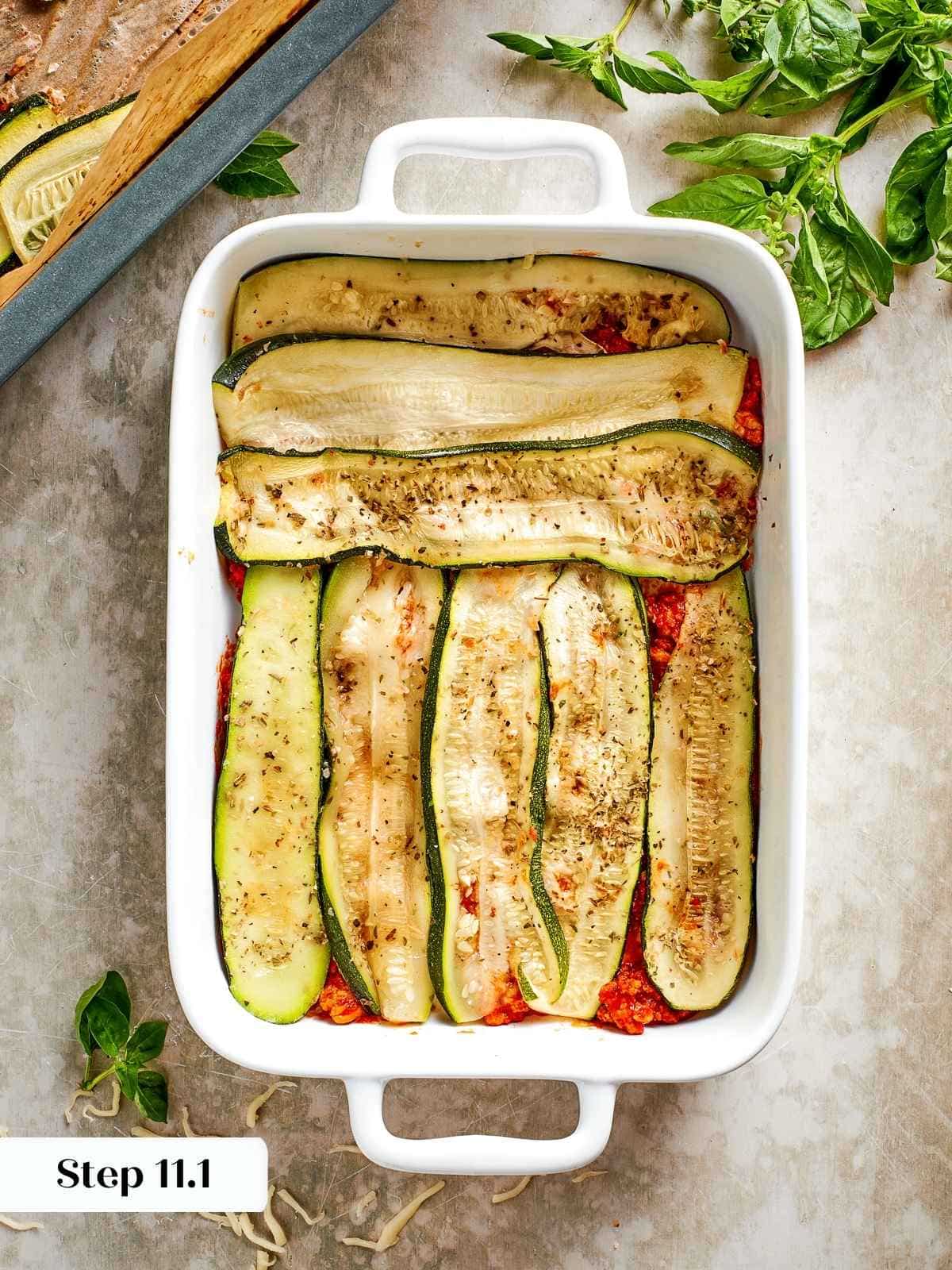 Thin roasted zucchini slices being layered as the base of the lasagna.
