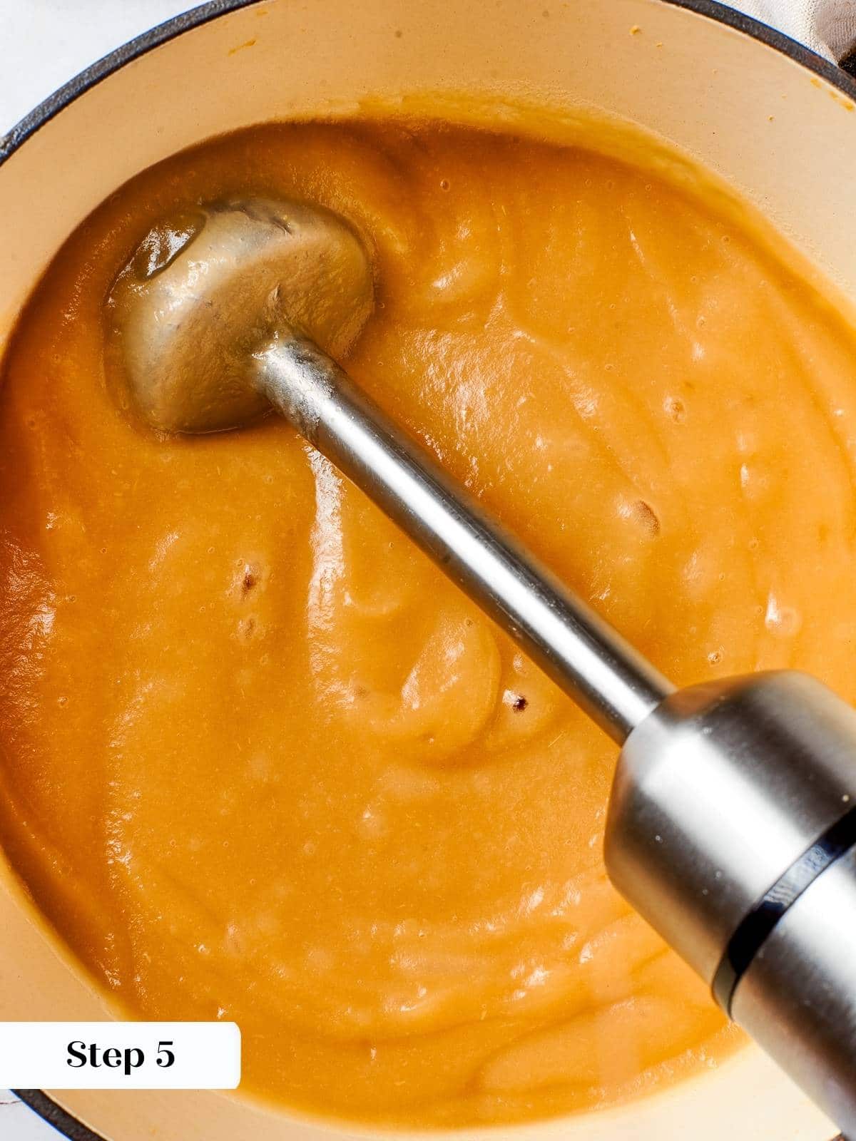 Immersion blender pureeing cooked apples directly in the pot to achieve smooth applesauce.