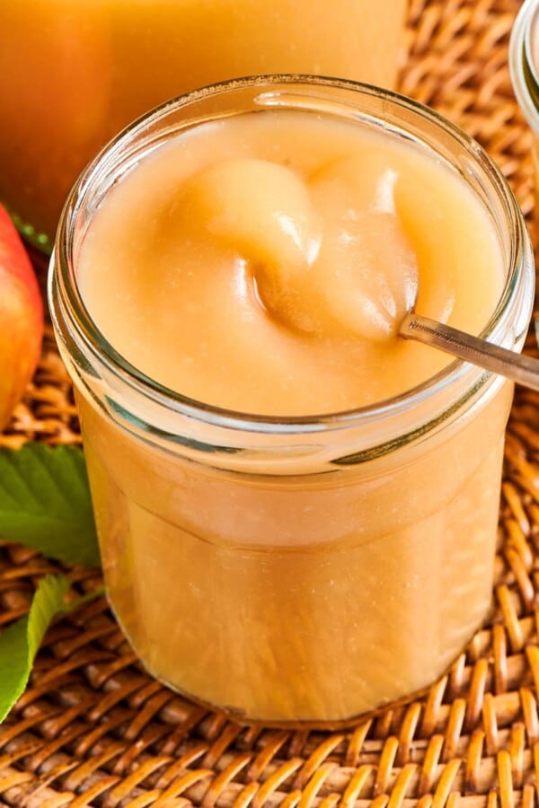 Homemade applesauce in a jar resting on a wicker placemat, surrounded by natural autumn light.