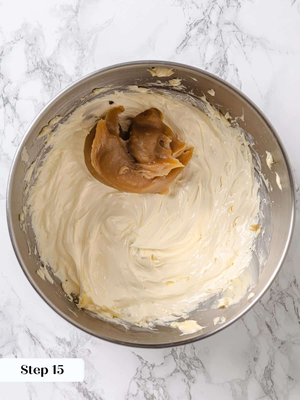 Thick frosting base mixture spooned into mixing bowl with whipped butter.