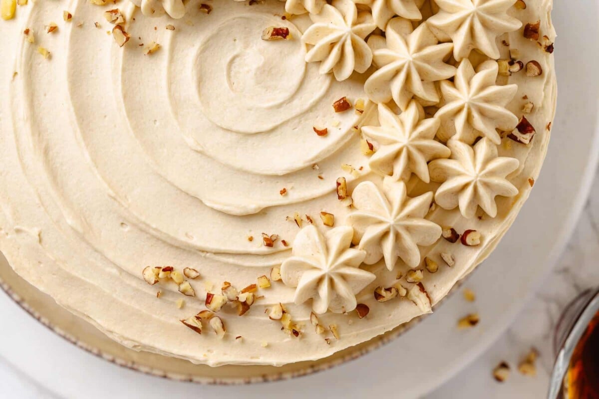 Maple frosting cake decorated with chopped nuts, adding crunch to creamy layers.