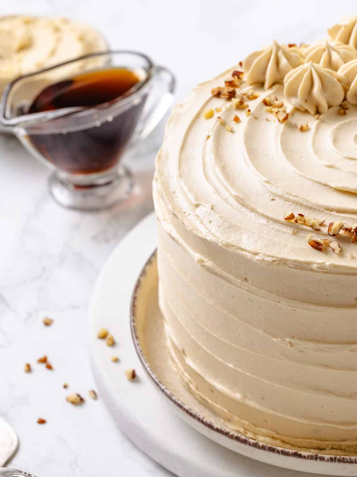 maple syrup next to frosting bowl, highlighting key ingredient in recipe.