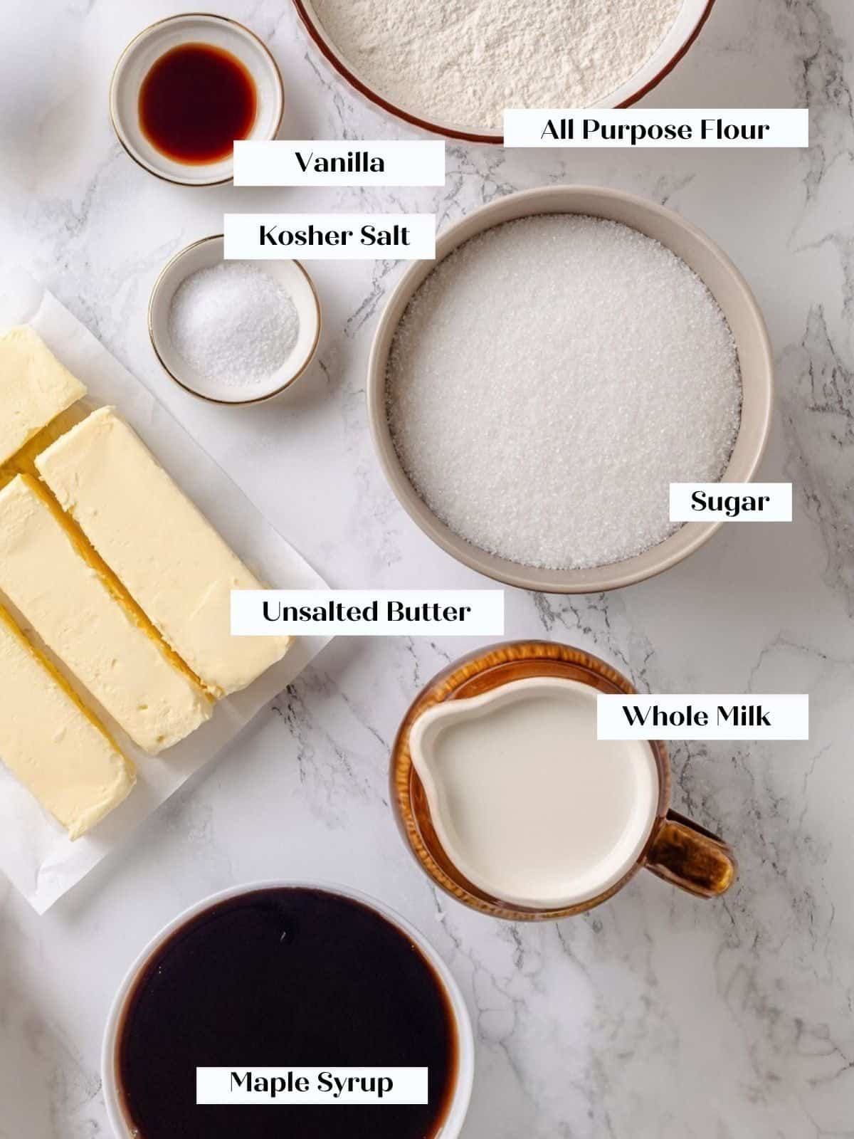 Ingredients for maple frosting arranged on a countertop including flour, sugar, milk, and syrup.