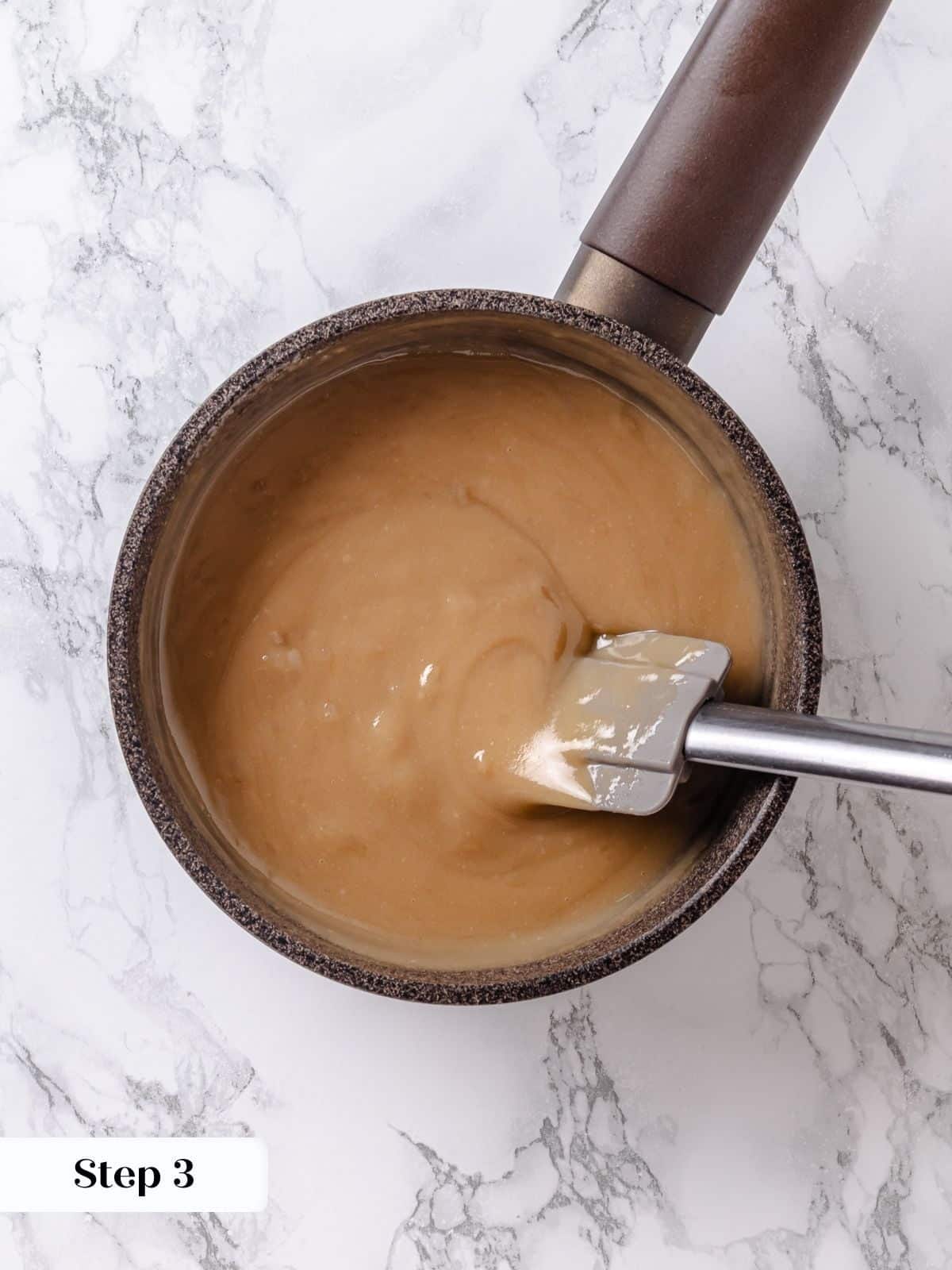 Maple frosting base being scraped with spatula across saucepan to prevent burning.