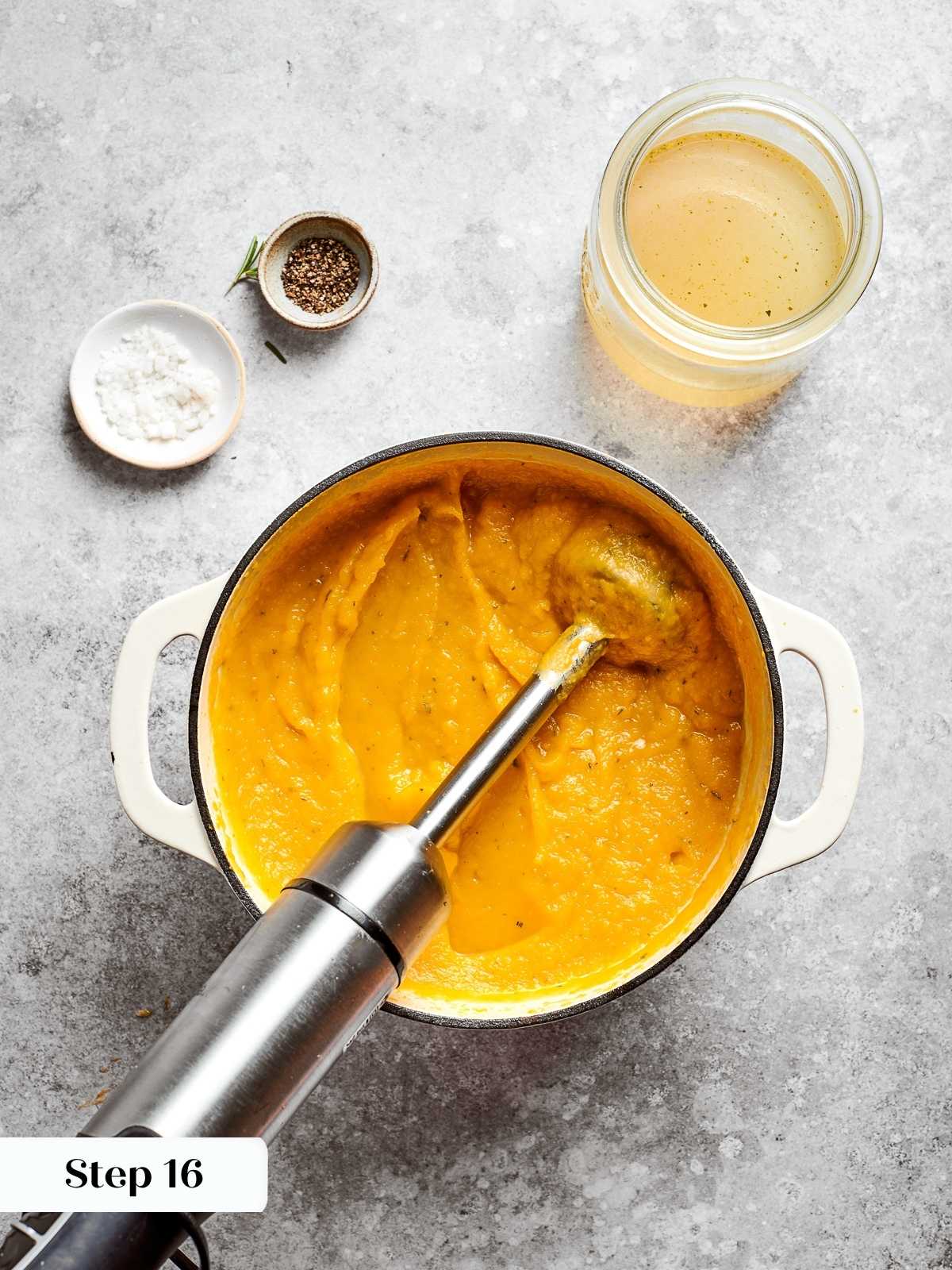 Immersion blender pureeing squash soup until creamy and smooth in the pot.
