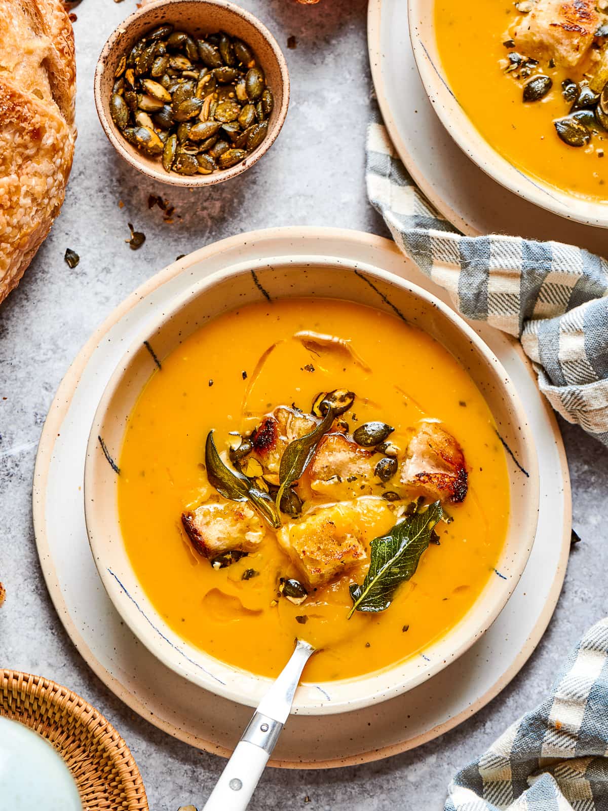 creamy squash soup in a bowl, garnished with black pepper and herbs.
