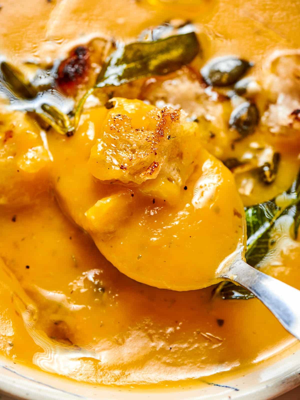 A spoon dipping into rich squash soup, showing its creamy thickness and warmth.