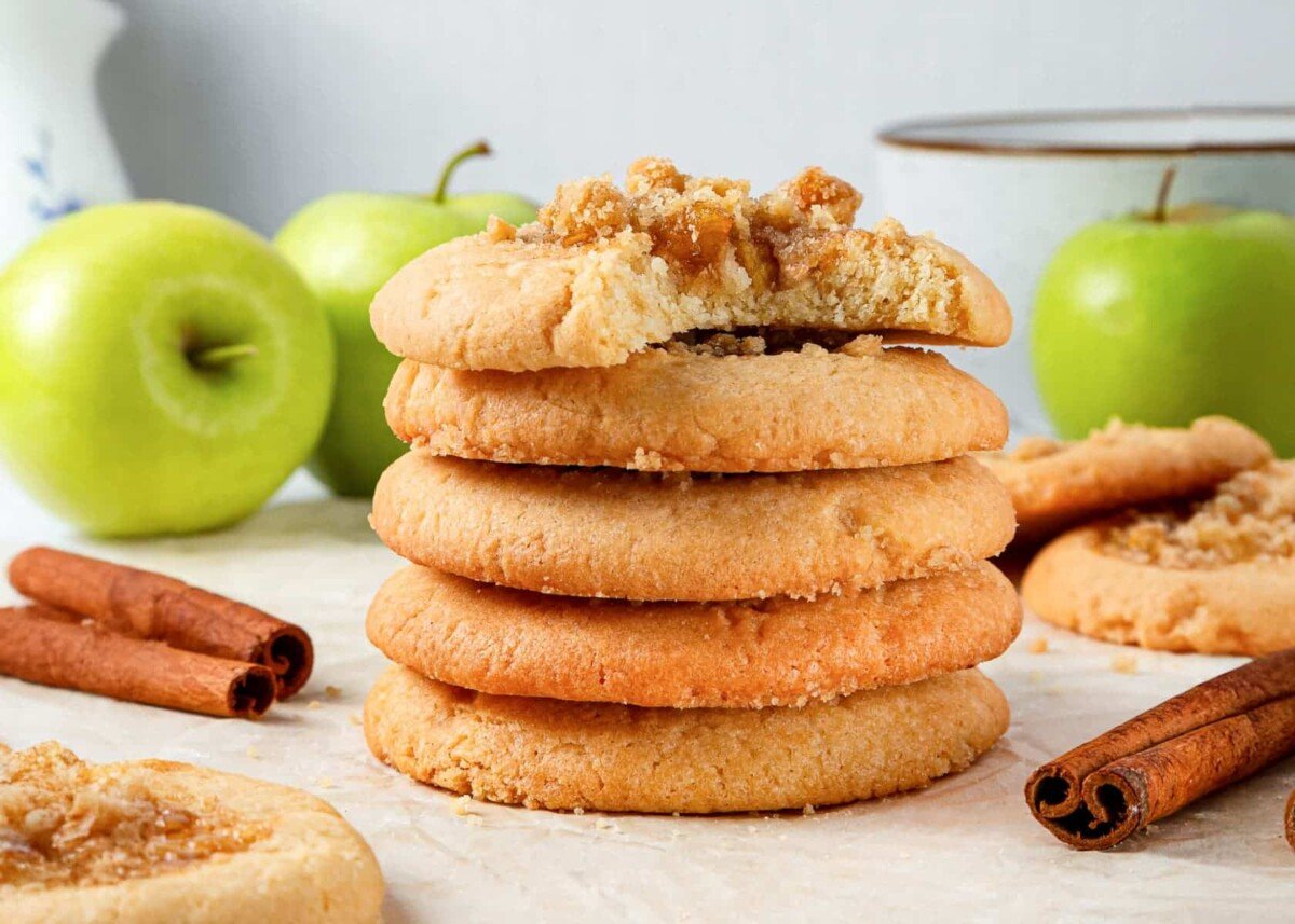 Baked apple pie cookies displayed beside whole green apples and cinnamon sticks for garnish.