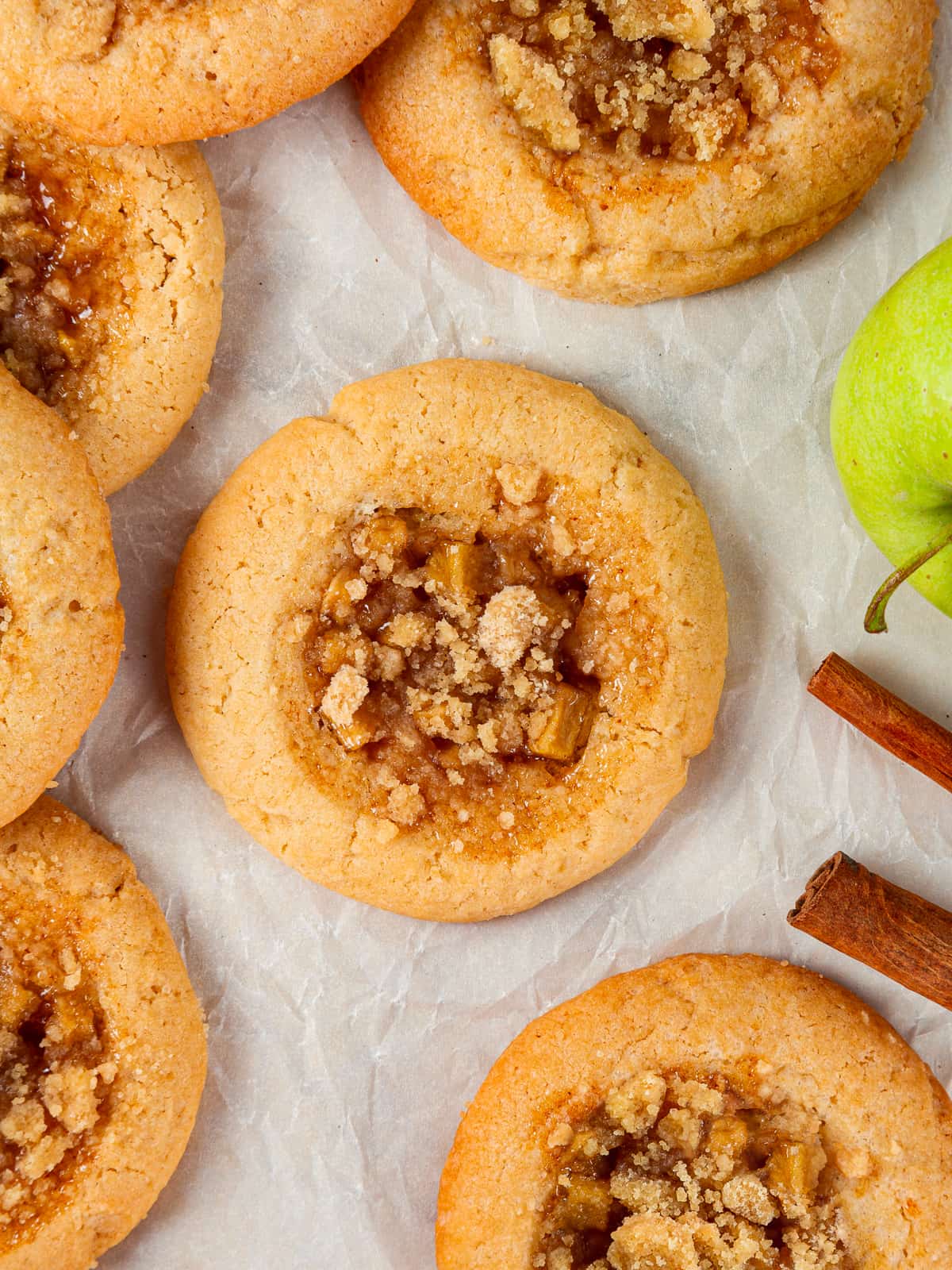Baked apple cookies with visible crumble and caramelized apple filling on a parchment sheet.