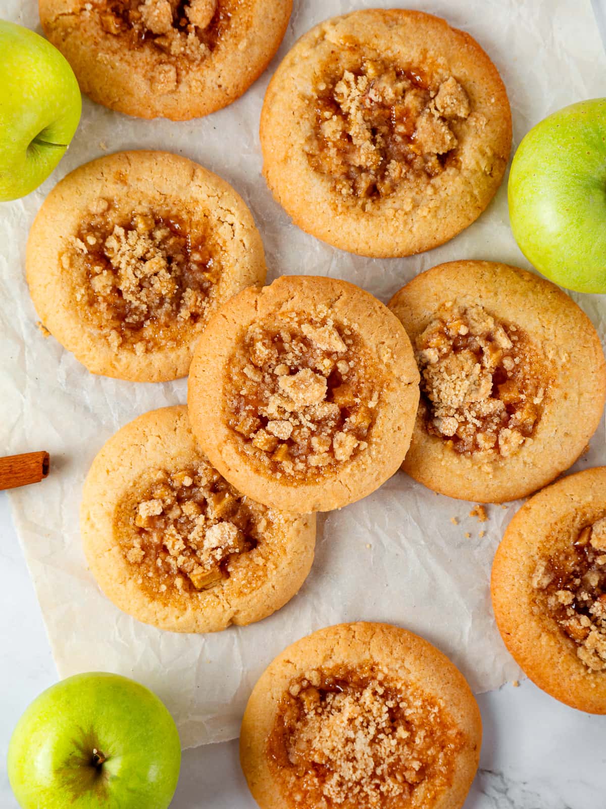Assorted apple pie cookies spread on a table showing golden crumble tops and soft centers.