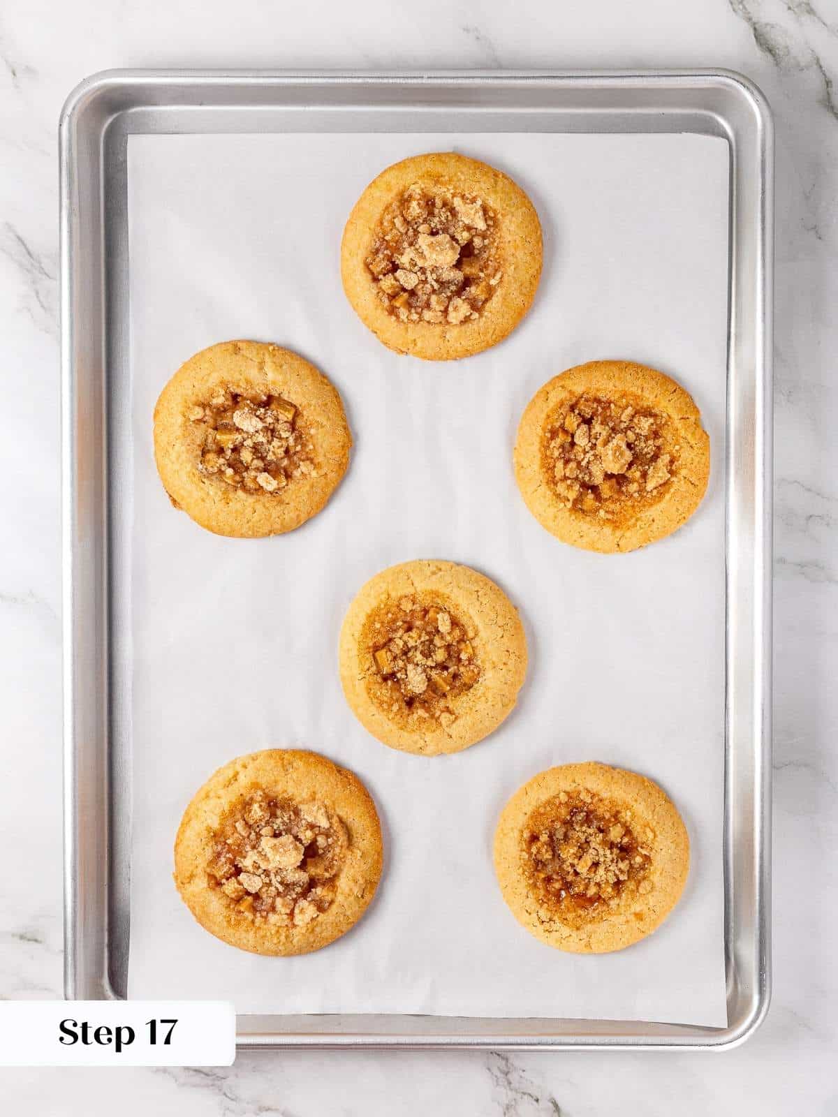 Freshly baked apple pie cookies cooling on a parchment-lined baking sheet after the oven.