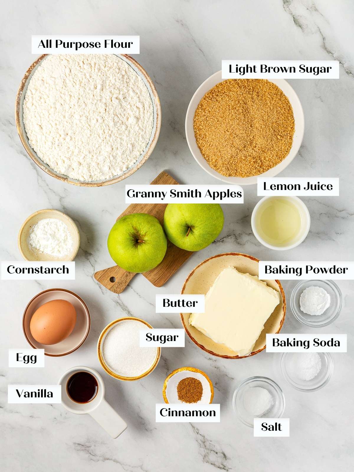Baking ingredients for apple pie cookies arranged on a kitchen counter, including apples, flour, and butter.