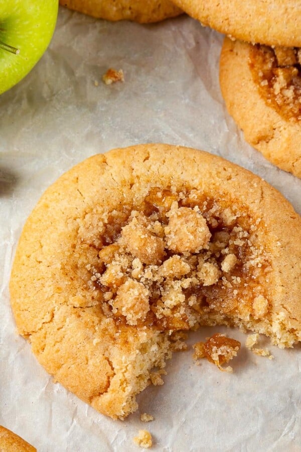 A single apple pie cookie with a bite revealing its chewy brown sugar dough and apple filling.