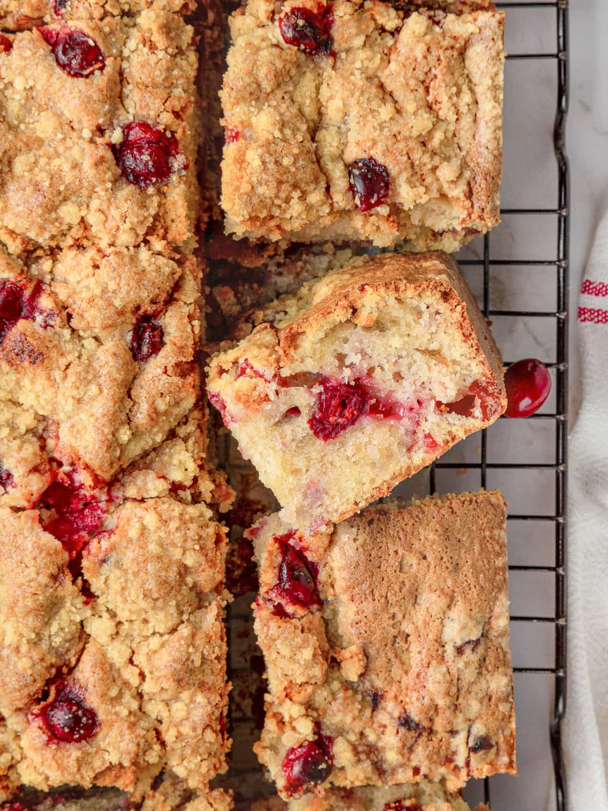Cranberry cake resting on a cooling rack after baking with streusel crumbs scattered below.