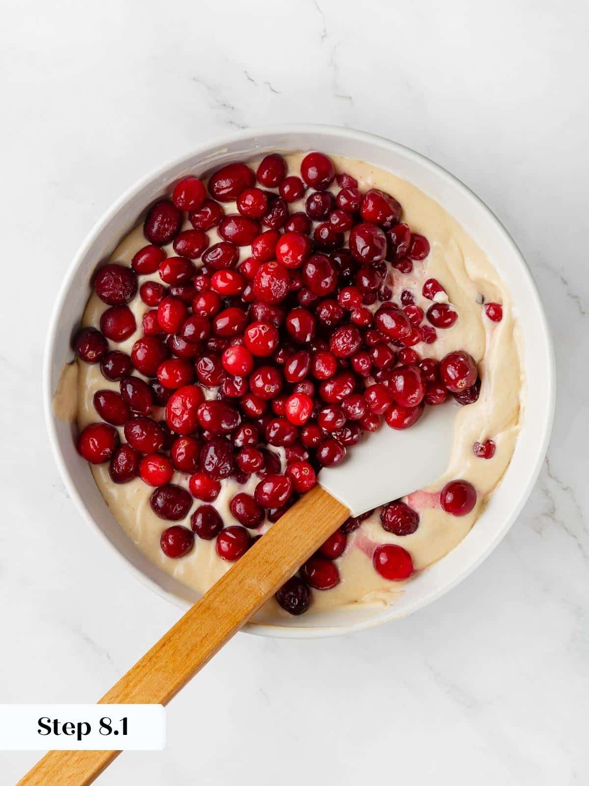 Fresh cranberries being folded into light cake batter with a spatula.