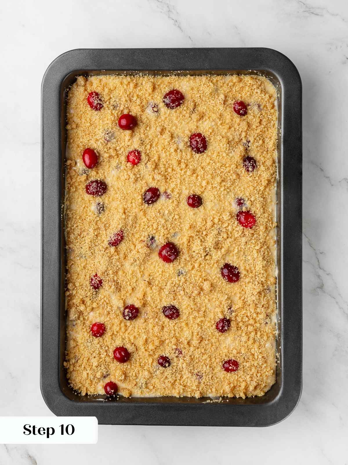 Cake batter topped with brown sugar streusel before baking, showing bright cranberries on top.