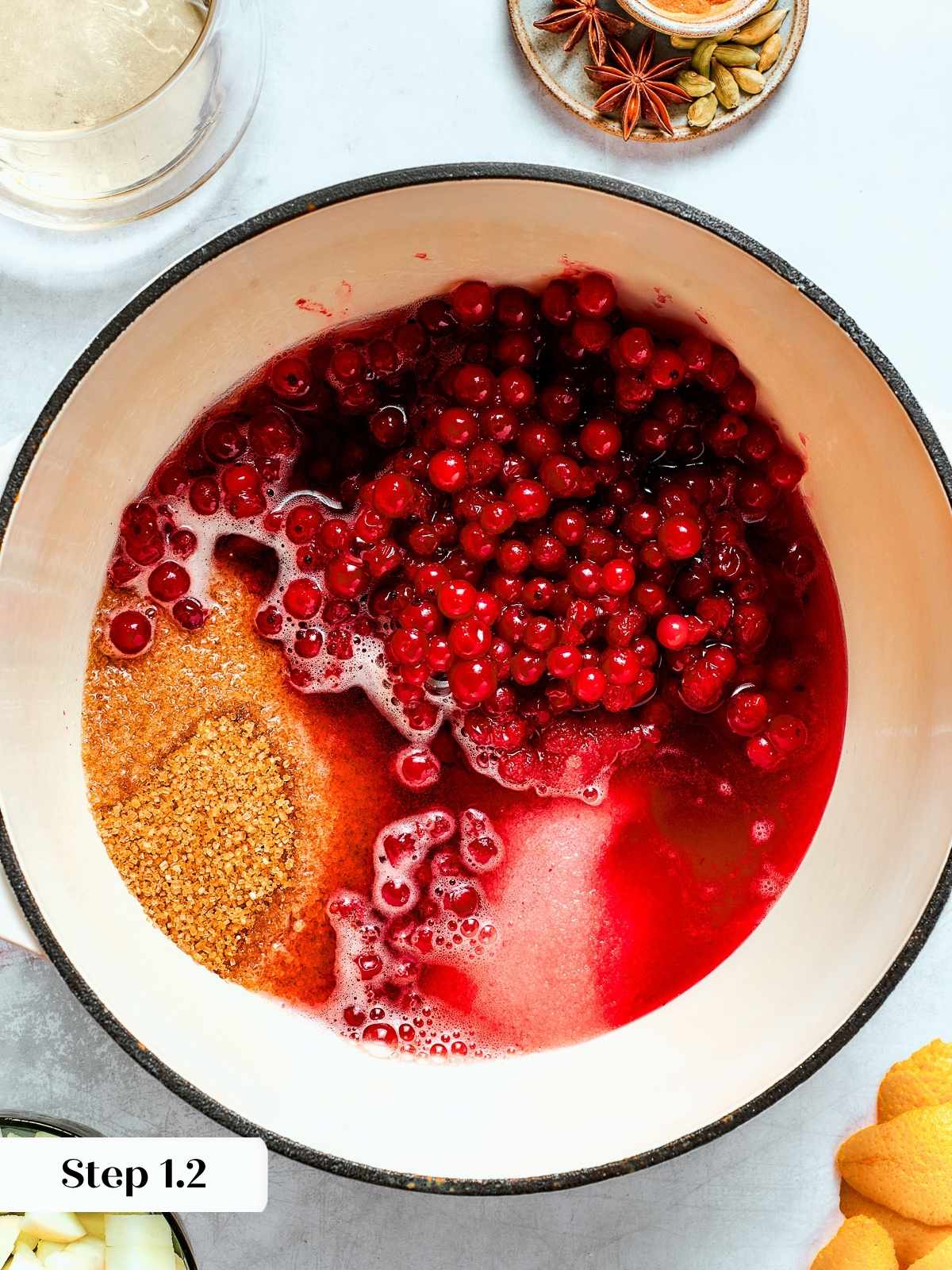 Cranberries, sugar, and apple cider bubbling together in a saucepan creating a fragrant spiced sauce.