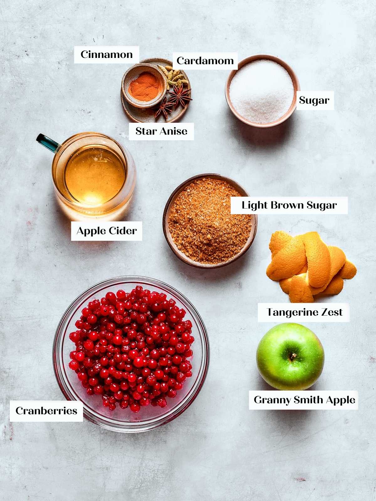 Measured ingredients for cranberry sauce including cranberries, apple, cinnamon, and brown sugar on a kitchen counter.