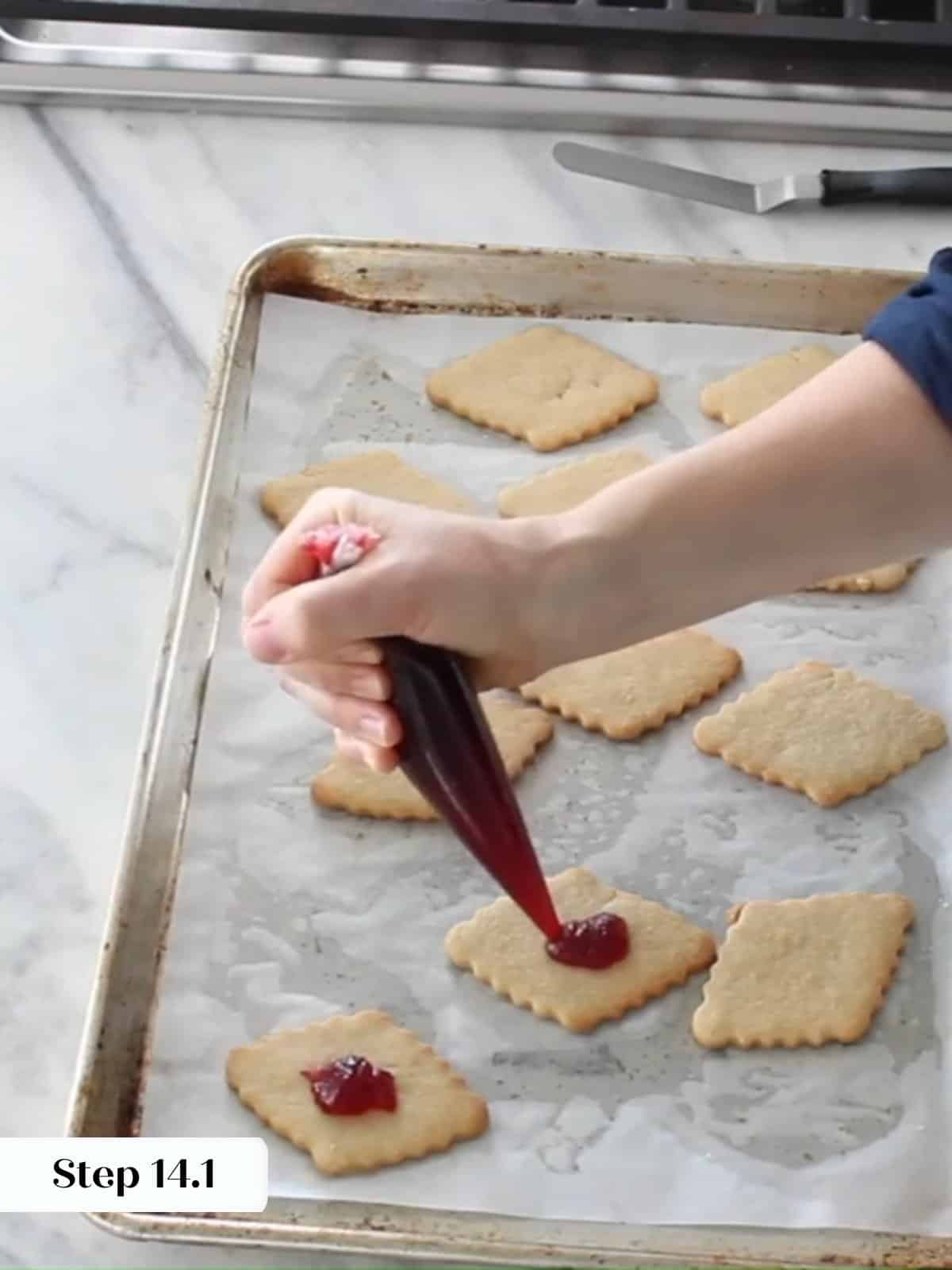 Raspberry preserves being piped onto the flat side of cookie bottoms before sandwiching.