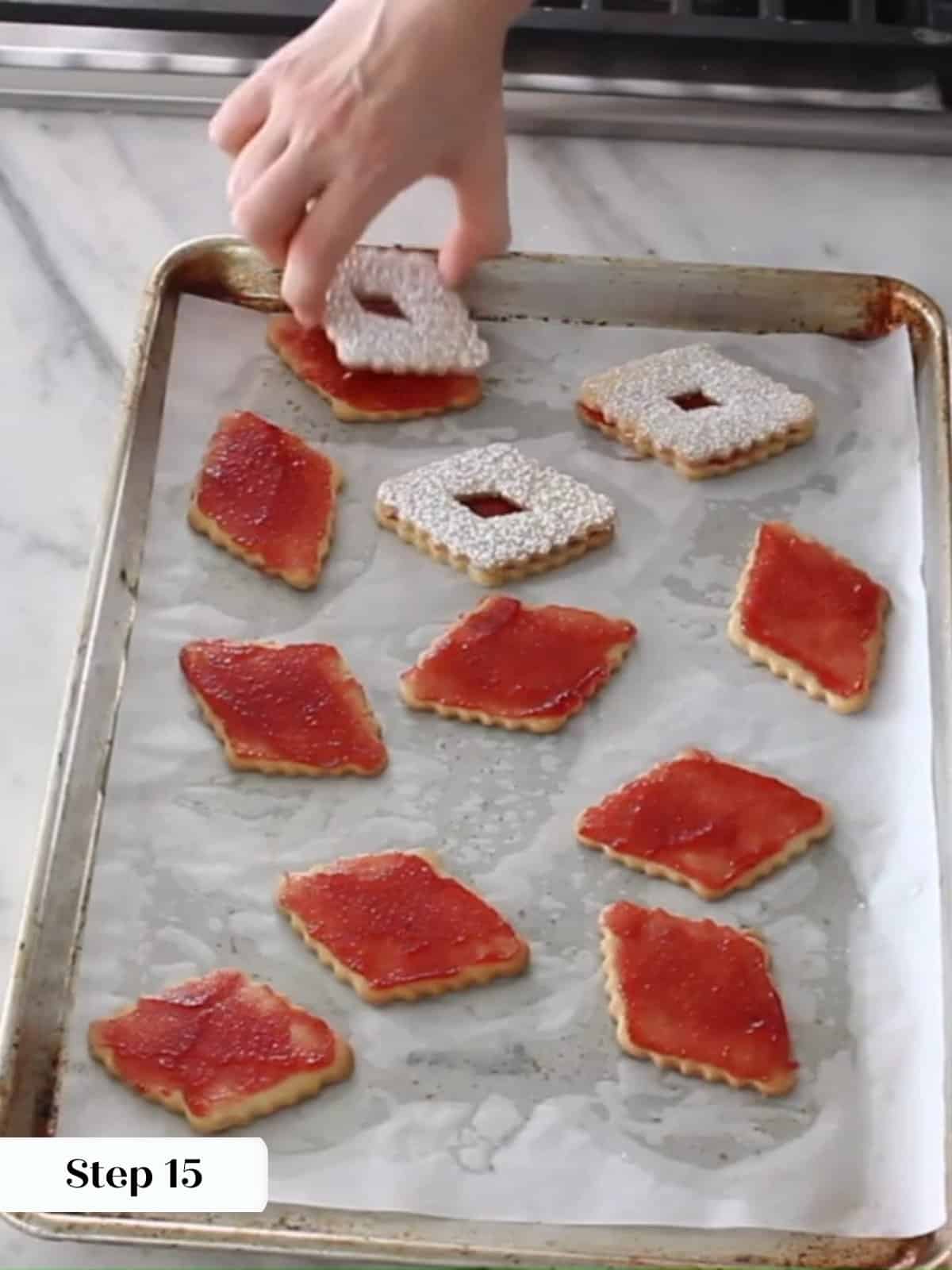 Assembled Linzer cookies being finished with top halves showing jam through the center cutouts.
