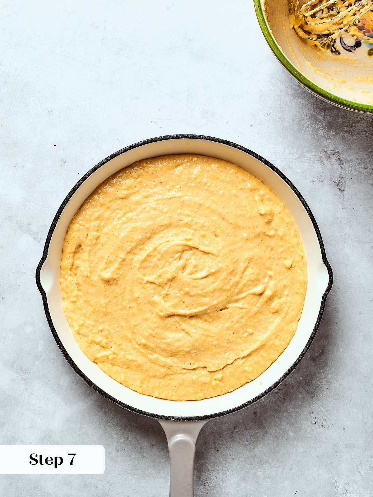 Smooth cornbread batter spread evenly in a cast iron skillet before baking.