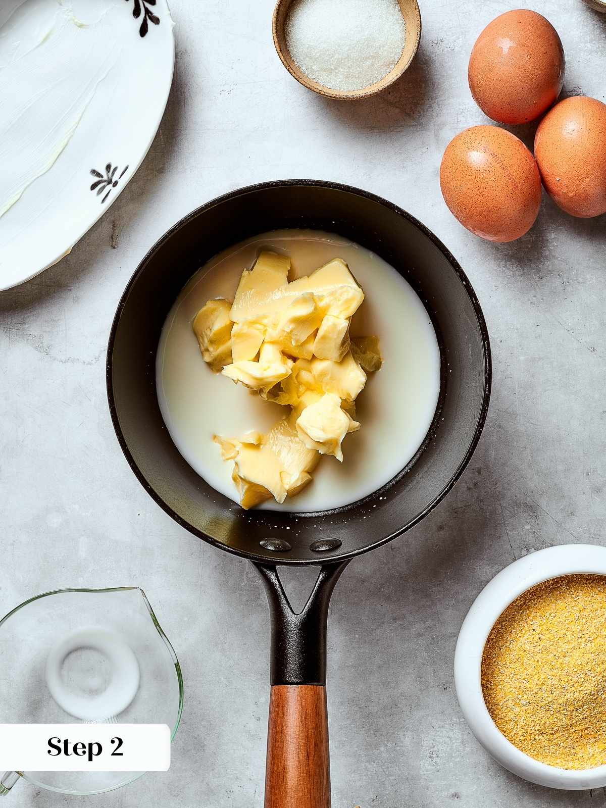 Saucepan with melted butter and warm milk being stirred together on a stovetop.