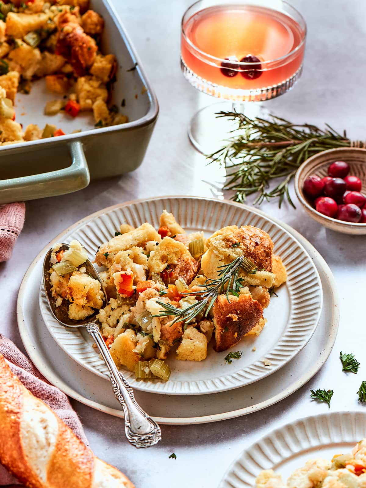 Serving dish filled with cornbread dressing beside cranberries and seasonal herbs for presentation.