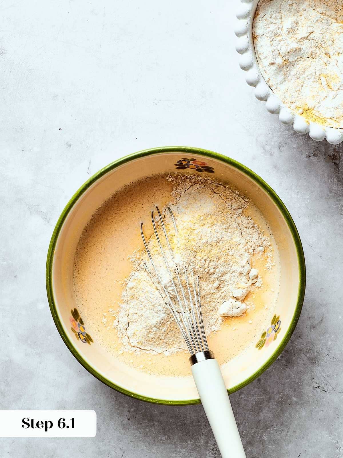 Dry ingredients being added to wet mixture while whisking to form a smooth cornbread batter.
