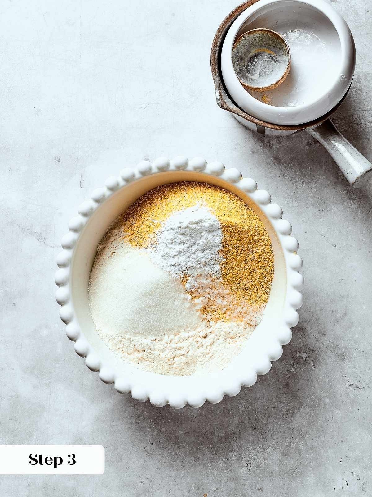 Cornmeal, flour, and salt being whisked together in a bowl to combine the dry ingredients.
