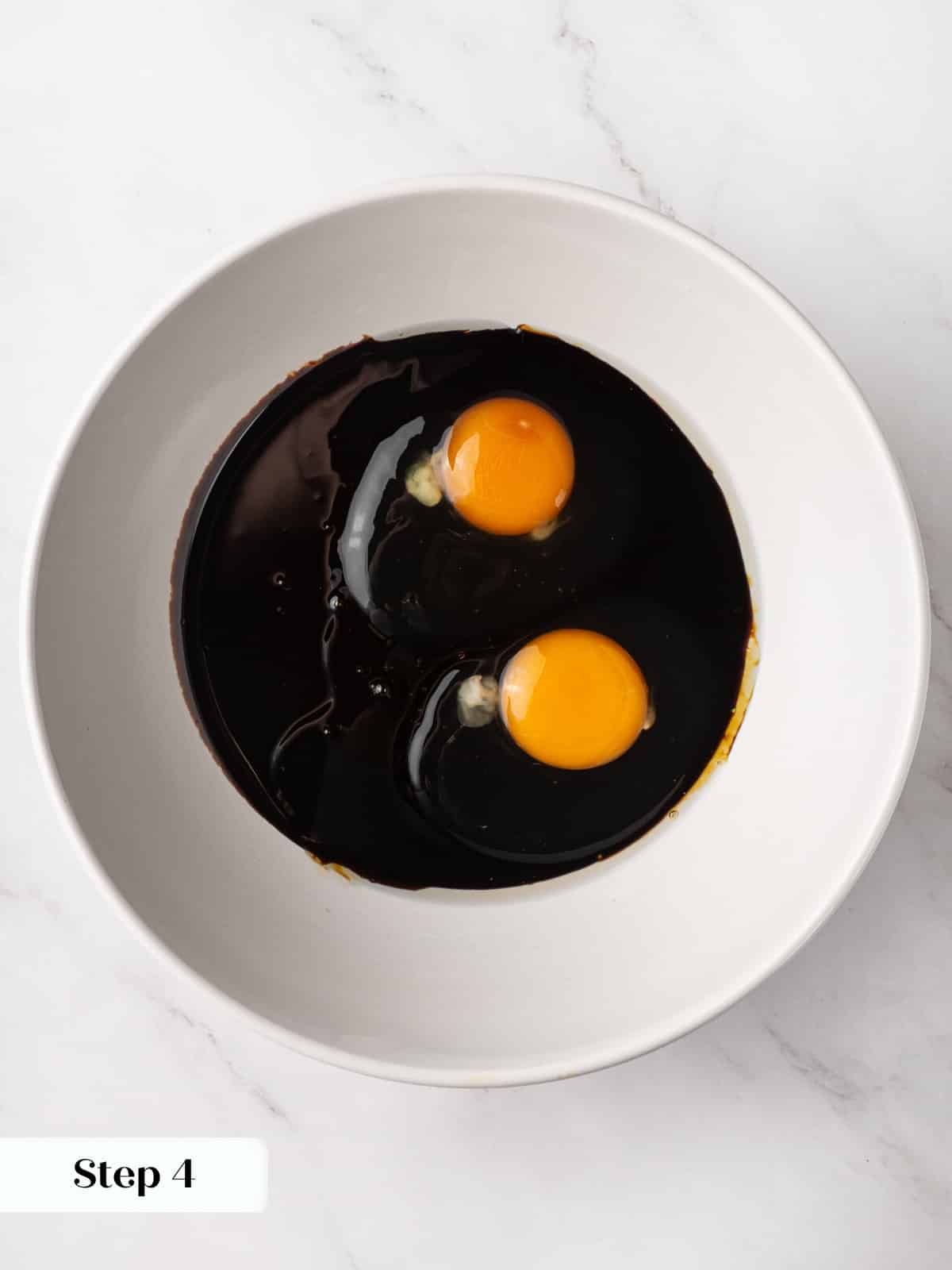 Dark molasses sitting with cracked eggs in a bowl before whisking together.