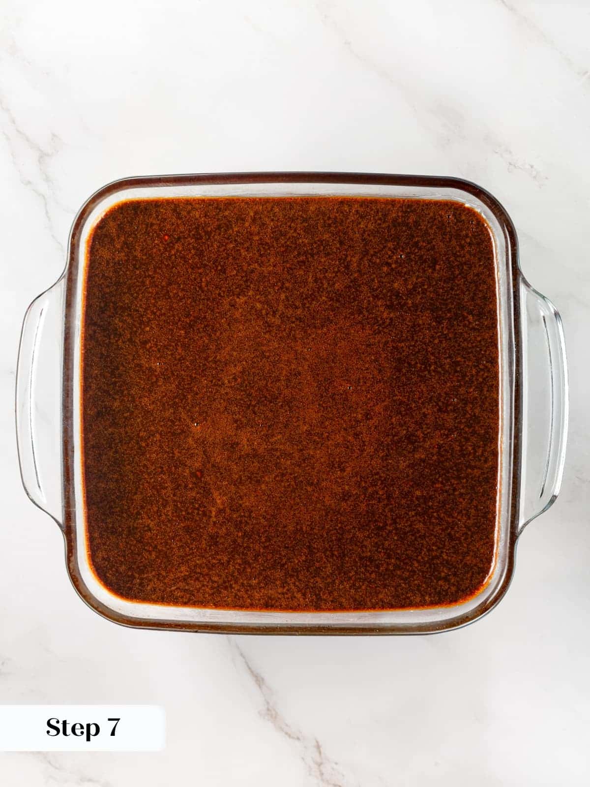 Gingerbread cake batter being poured into a rectangular baking dish lined and prepared.