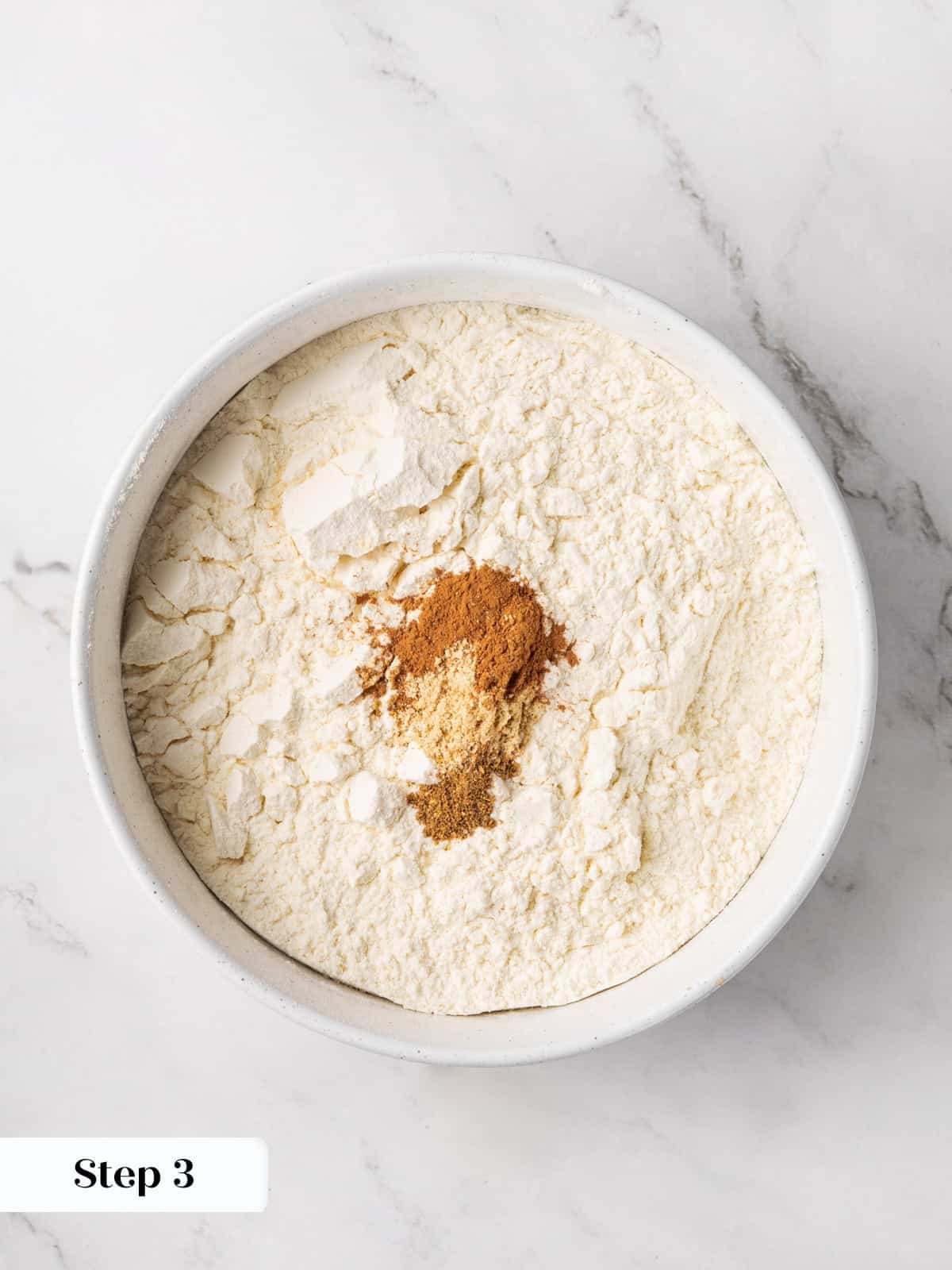 Dry ingredients for gingerbread cake, flour whisked with ginger, cinnamon, and allspice in a bowl.