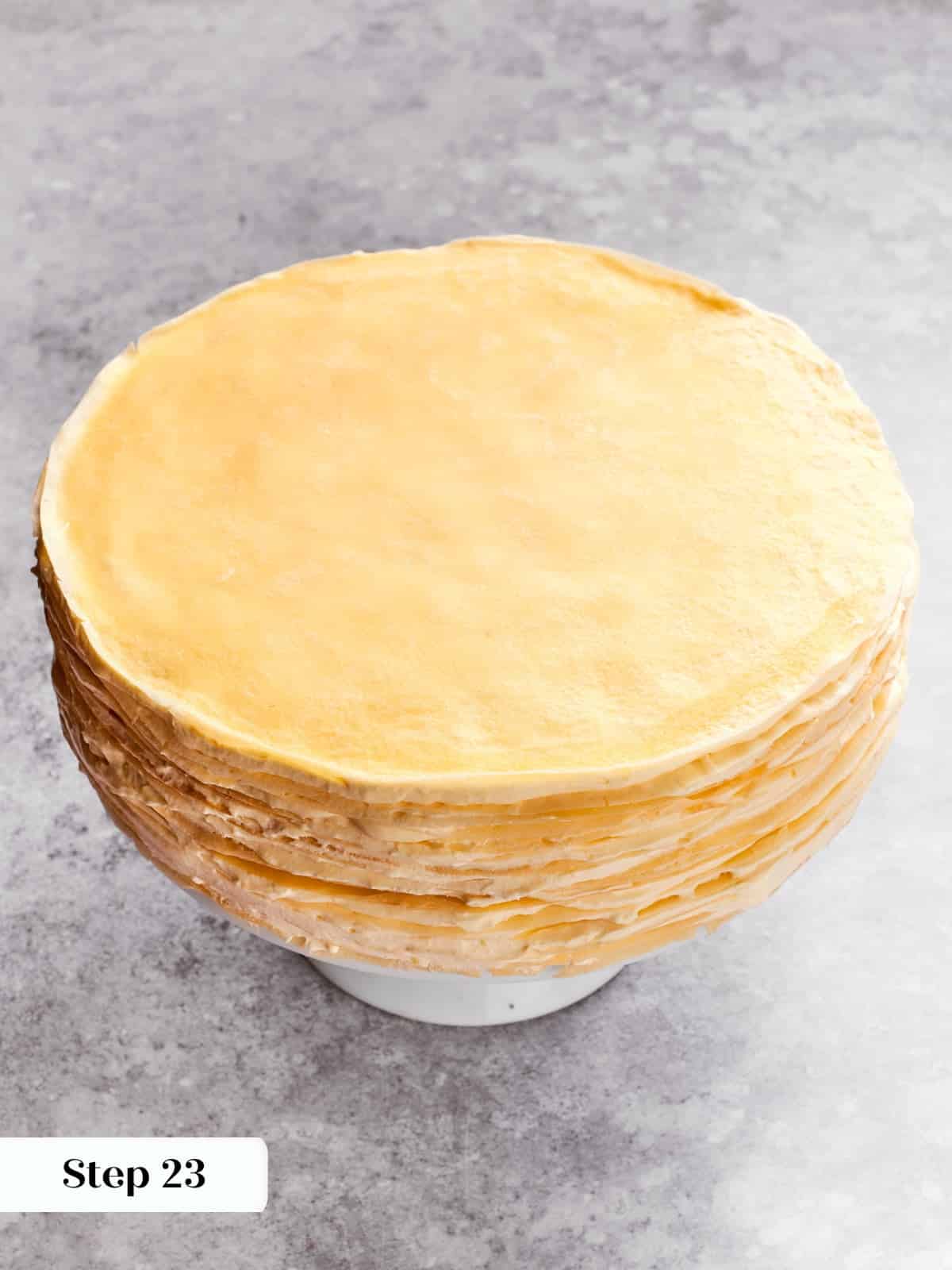 Crepes being layered with crème légère to build the tall mille crepe cake.