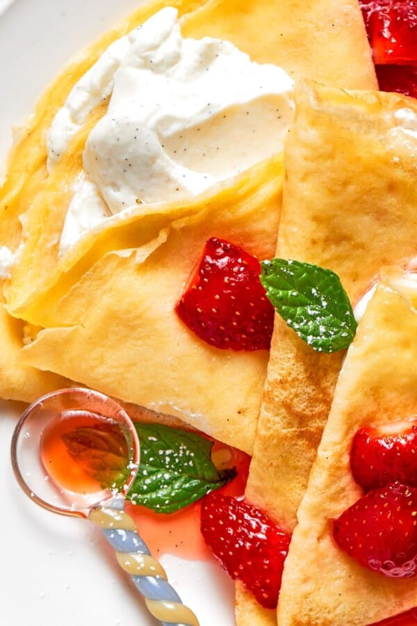 A plate of cream-filled crepes layered with fresh strawberries and golden folds.