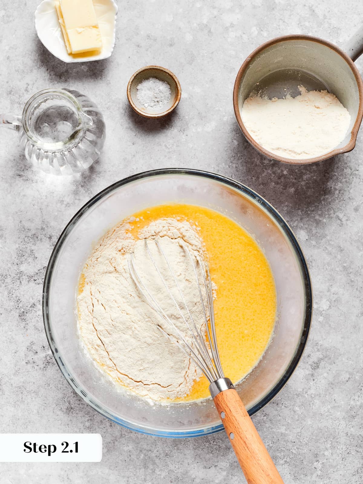 Flours being whisked slowly into the wet mixture to form a smooth crepe batter.