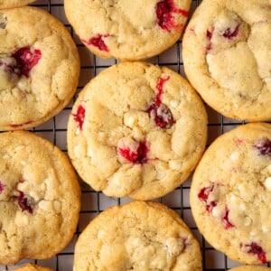 Freshly baked cookies cooling on a wire rack with cranberries and white chocolate throughout.