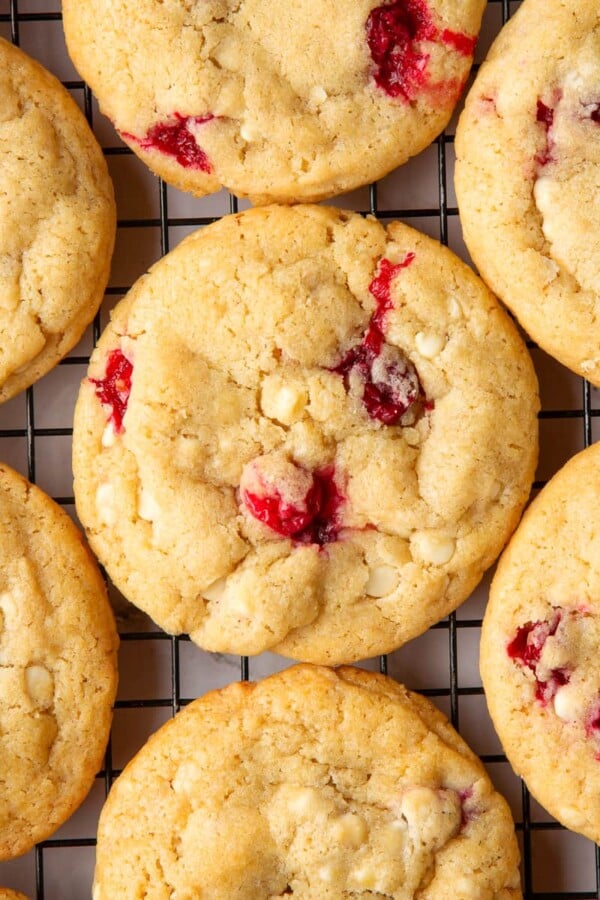 Freshly baked cookies cooling on a wire rack with cranberries and white chocolate throughout.