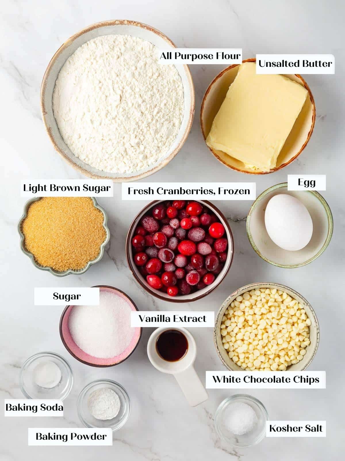 All cookie ingredients including butter, eggs, cranberries, and white chocolate laid out on a countertop.