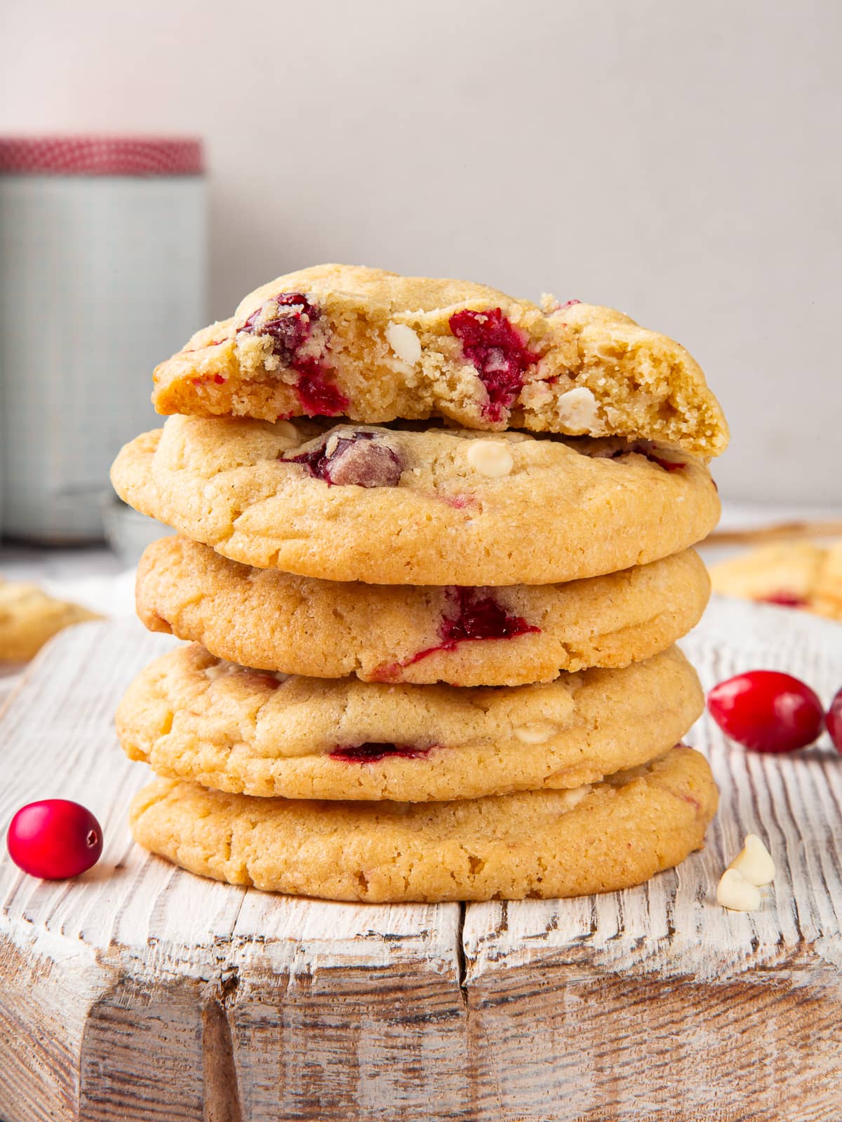 Baked cookies surrounded by scattered cranberries and crumbs on a neutral surface.