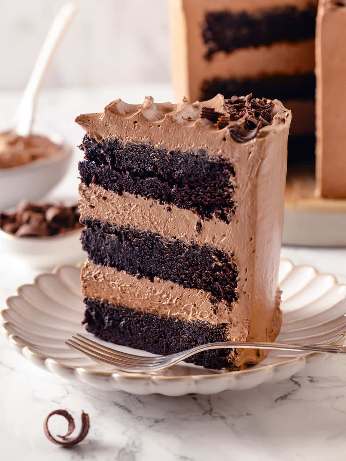 A slice of chocolate cake with tidy buttercream layers served beside a simple fork.